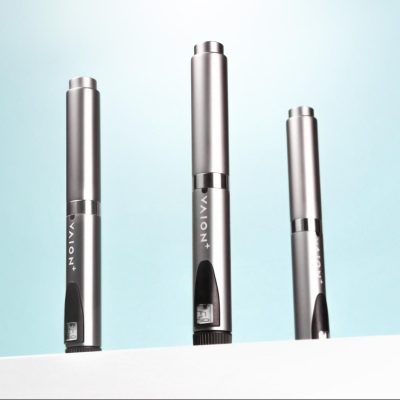 Three VAION+ PEN devices are displayed upright against a light blue background. Each pen has a sleek, metallic design with a black clip and the brand name "VAION+" visible on the side. The pens are positioned on a white surface.